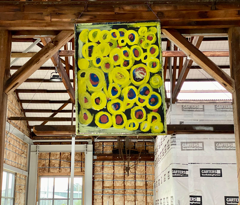 a larges colourful painting of circles hanging from a beam high up in a warehouse space