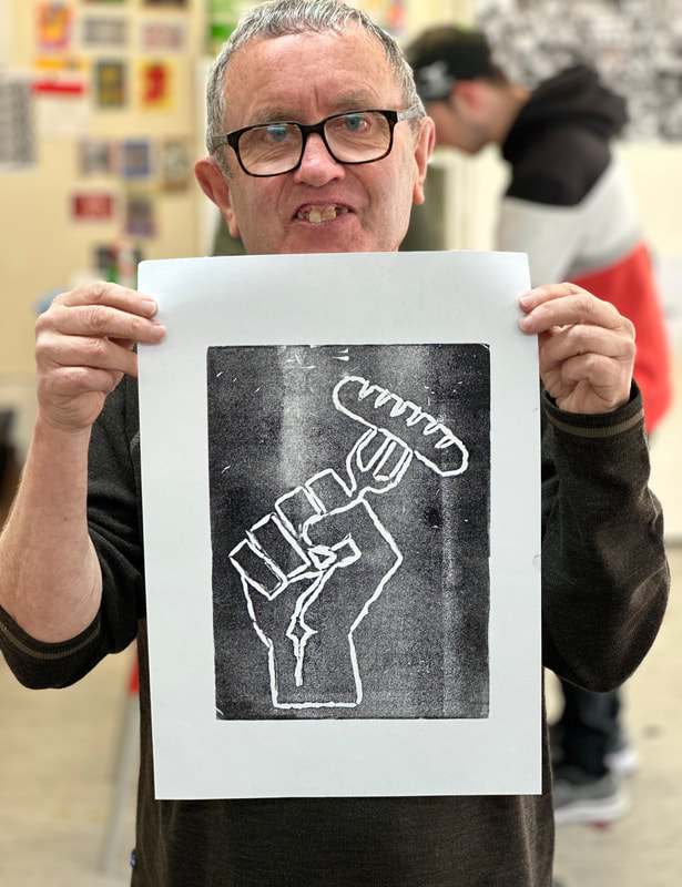 A man holding a sheet of paper with a printed image of a hand holding a fork with a sausage on it.