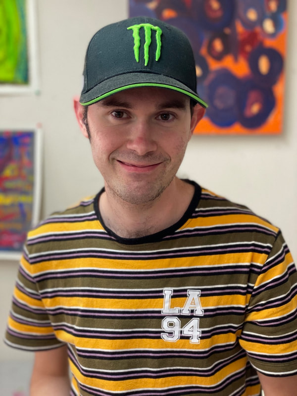 Photograph of artist Jordan Taw in a baseball cap smiling at the camera